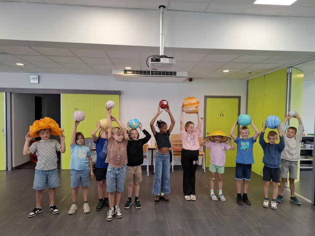 Kinderen staan op een rij en tonen planeten. 